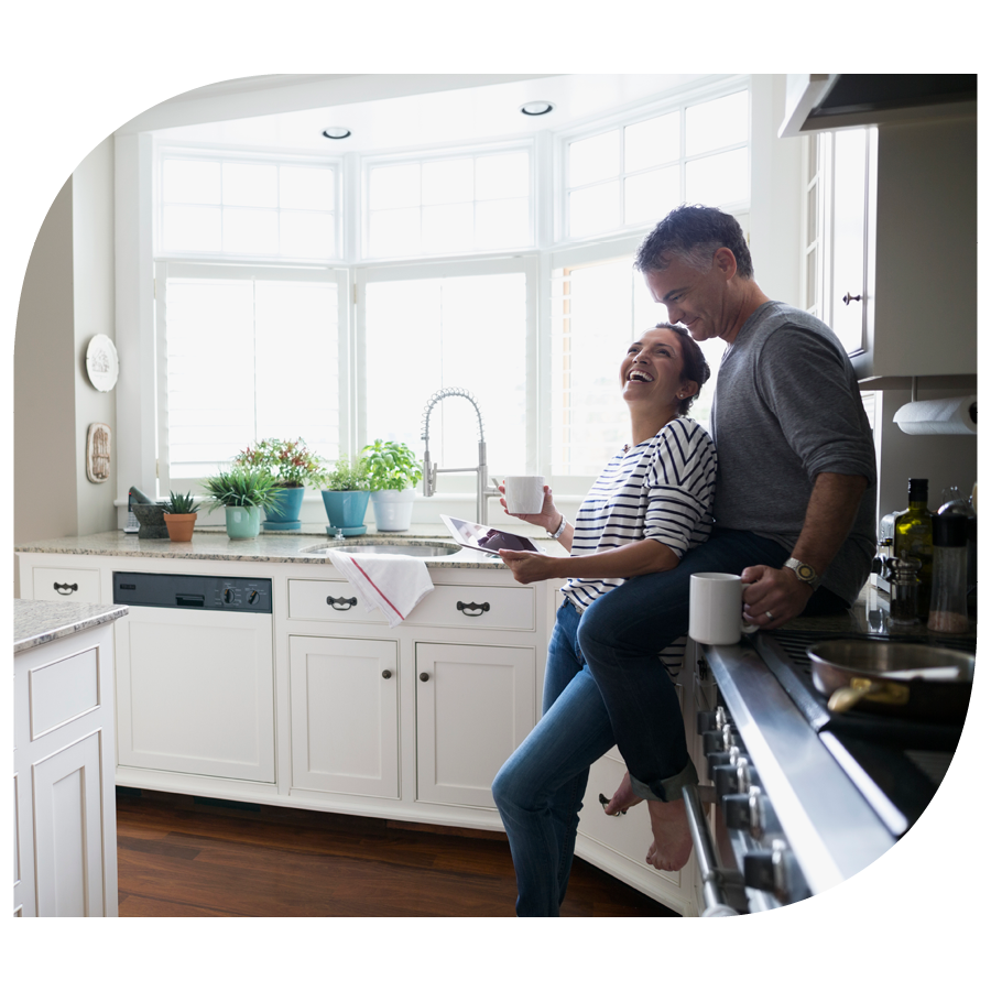 couple laughing and drinking coffee in home kitchen looking at tablet